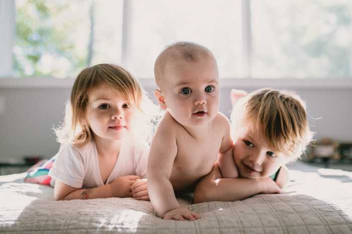 three small siblings snuggling in bed with light coming in the window behind them during a family photo shoot
