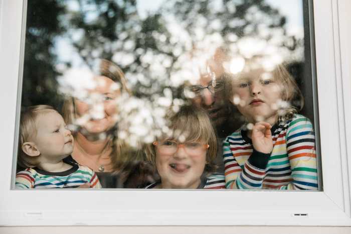Family photo of three kids and adult taken from outside a window making funny faces steaming up the glass