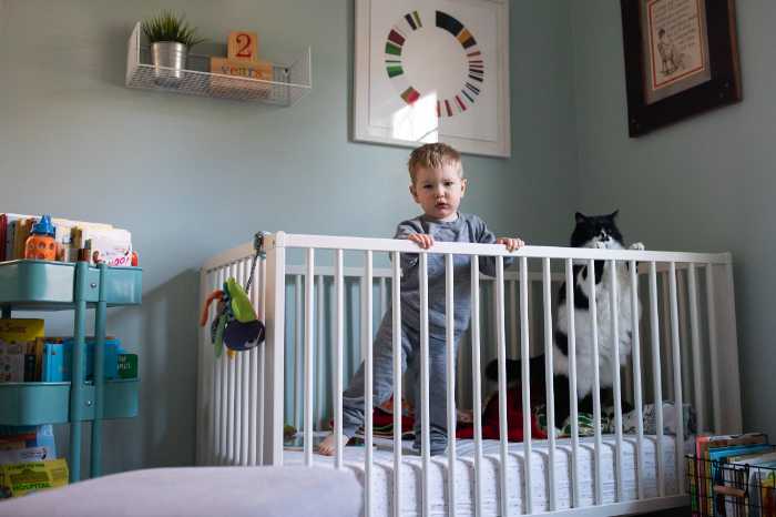 Small toddler standing in crib with black and white cat standing next to him family photo shoot