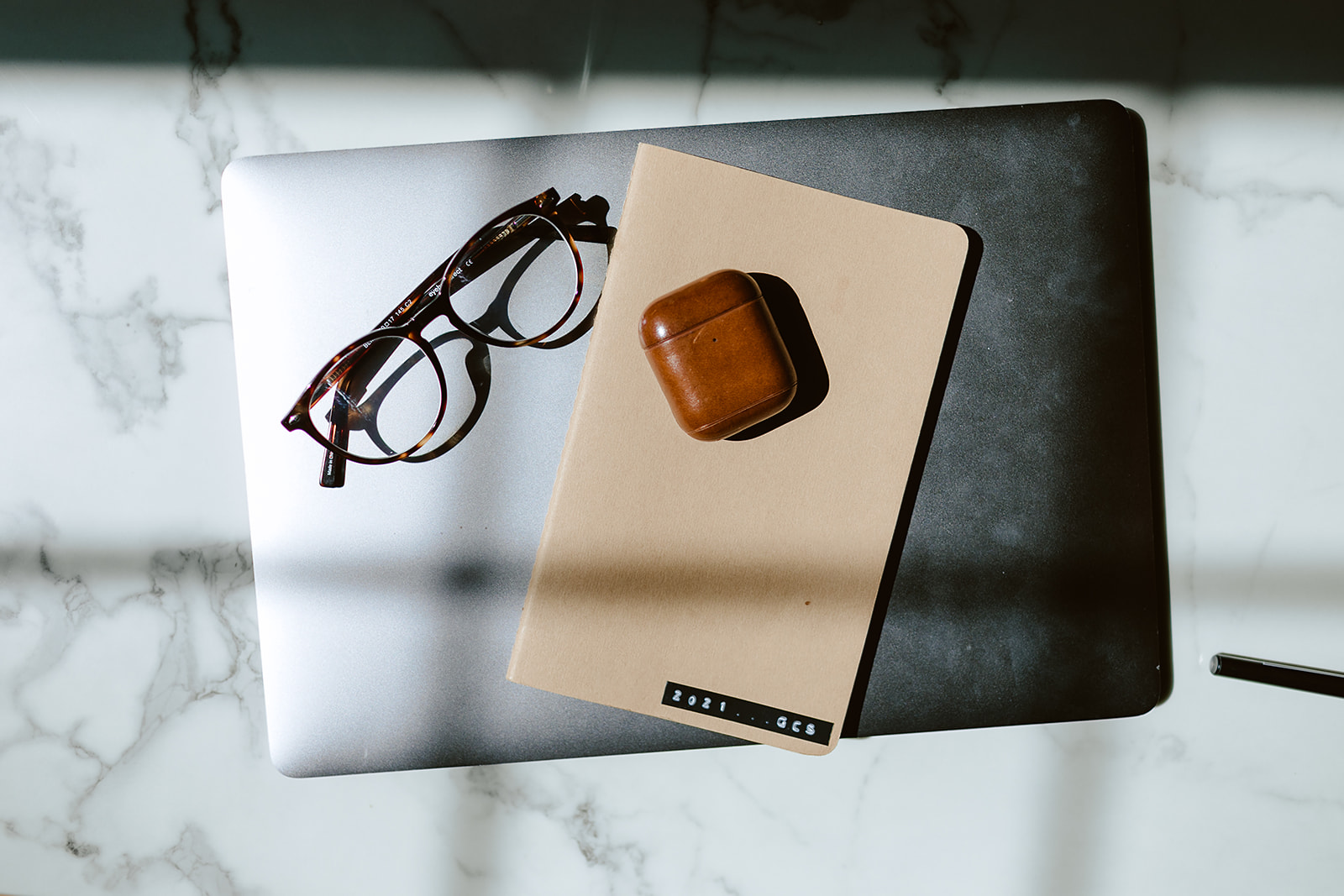 closed laptop with notebook, glasses and airpods case on top