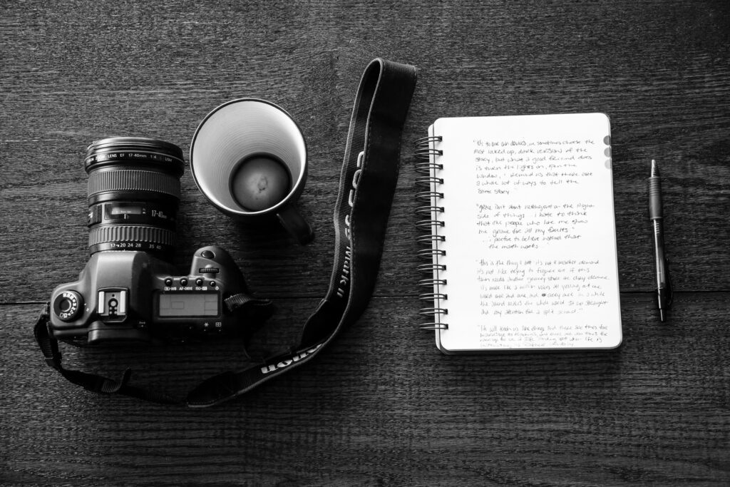 table with dslr camera, empty coffee cup, notebook and pen